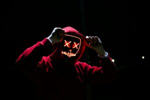 pexels-photo-1097456-1097456 - Rockstar Recruiting Group A spooky illuminated mask figure with a red hoodie in a dark setting, perfect for Halloween themes.